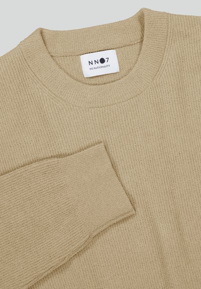 Beige geribbeld trui met een ronde halslijn, met een subtiele textuur. Etiket leest "NN07" met daaronder "No Nationality".