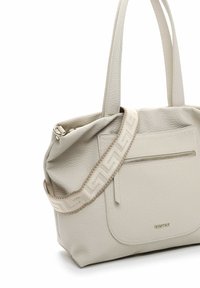 Light beige leather tote bag with double handles, textured surface, front zip pocket, and decorative patterned strap. Features gold logo accent.