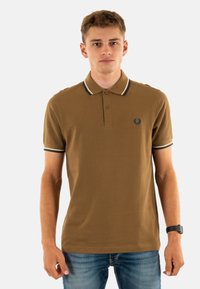 Bruine poloshirt met een tweeknopssluiting, geribde kraag en manchetten met zwart-witte strepen. Inclusief een logo op de linkerborst.