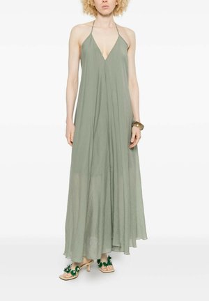 Vrouw draagt een losse, mouwloze maxi-jurk in saliegroen met halternek, een brede armband en open-toe hakken met groene bloemaccenten.