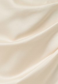 Tissu en satin crème, lisse et fluide, présentant de doux plis et un éclat réfléchissant subtil.