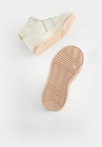 Baskets montantes blanches en matériau synthétique avec une semelle en caoutchouc texturé, dotées d'une sangle Velcro et d'accents lisses.