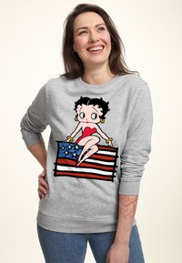 Sudadera gris con un dibujo de Betty Boop sentada sobre una bandera estadounidense. El diseño incluye colores rojo, azul y blanco con contornos distintivos.