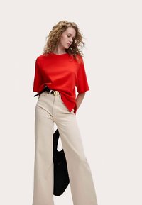 Röd topp med korta ärmar kombinerad med beiga vida byxor med hög midja, utrustade med ett svart bälte med ett runt guldfärgat spänne och en svart väska med struktur.