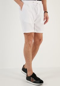 Witte, gemêleerde shorts met een elastische tailleband en zijzakken, gecombineerd met zwarte sneakers met een gestreept patroon en logoaccent.