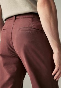 Pantalones entallados burdeos con una textura suave, que presentan dos bolsillos traseros y una silueta ajustada.