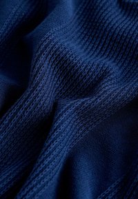 Tissu tricoté bleu marine présentant des motifs texturés avec des mailles lisses et ajourées alternées, créant un effet superposé.