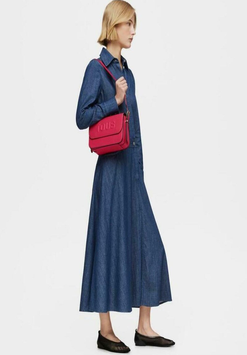 Vestido de mezclilla, largo y abotonado, en azul. Zapatos planos negros y un pequeño bolso bandolera de cuero rojo con logotipo de la marca en relieve. Diseño limpio y minimalista.