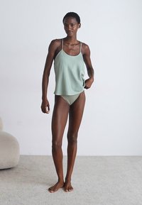 Lichtgroene camisole met dunne bandjes, gecombineerd met een bijpassende sheer groene bikini onderbroek. Gladde stof, ruime pasvorm en eenvoudig ontwerp.