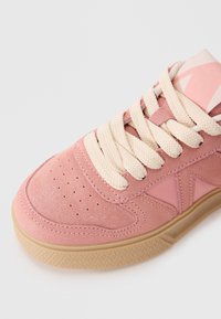 Pink suede sneaker featuring a textured surface, cream laces, and a rubber sole with a diamond pattern, showcasing a contemporary design.