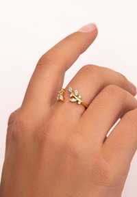 Guldringar med blommotiv har marquise-skarpade klara ädelstenar. En ring är större med ytterligare dekorationer, båda visar en strukturerad ytfinish.