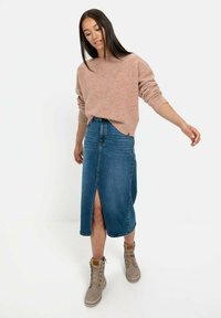 Roze gebreide trui met een losse pasvorm, gecombineerd met een knielange, blauwe denim rok met een split aan de voorkant en beige veterschoenen.