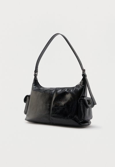 Μαύρη γυαλιστερή δερμάτινη τσάντα ώμου με έναν ρυθμιζόμενο ιμάντα και δύο πλαϊνές τσέπες με καπάκια, σε απλό φόντο.