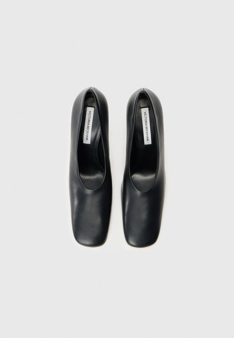 Schwarze Lederschuhe mit quadratischer Zehenform, flachem Absatz und glatter Textur. Das Innenlabel trägt die Aufschrift "Victoria Beckham." Einfaches und minimalistisches Design.