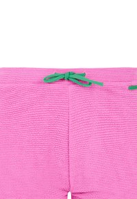 Shorts en éponge rose avec une surface texturée, dotés d'un cordon de serrage vert à la taille et d'un petit accent de marque.