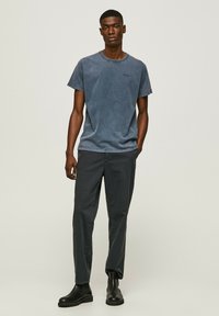 Blue cotton t-shirt with short sleeves and round neckline, paired with dark gray tapered pants and black ankle boots. Minimalist design.