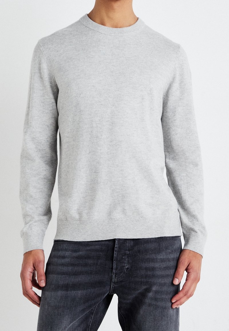 Pull ras du cou gris clair en tissu tricoté doux, avec des manches longues, des poignets côtelés et un ourlet droit. Associé à un jean en denim foncé.