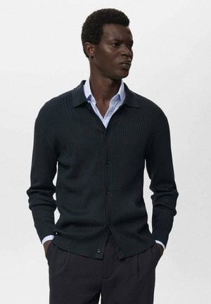 Dark green ribbed cardigan with a collar, button closure, and long sleeves, worn over a light blue shirt. Smooth texture and tailored fit.