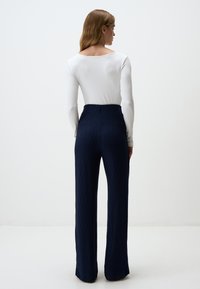 Pantaloni a coste navy lunghi con vita alta abbinati a un top bianco a maniche lunghe aderente, caratterizzato da un ampio scollo a barca. Vista da dietro.