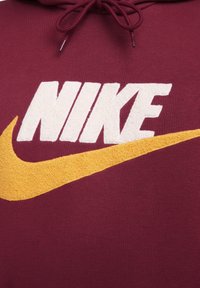 Sudadera color burdeos con un gran logo blanco de "NIKE" y un swoosh naranja, confeccionada en un tejido texturizado y suave para mayor detalle.