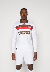 Hvit langermet fotballdrakt med brun krage og rød horisontal stripe. Har et "congstar"-logo og klubbmerke på brystet.