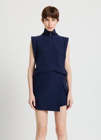 Marineblaues zweiteiliges Outfit mit einem ärmellosen Oberteil mit Stehkragen und Reißverschluss, kombiniert mit einem Minirock mit asymmetrischem Saum.