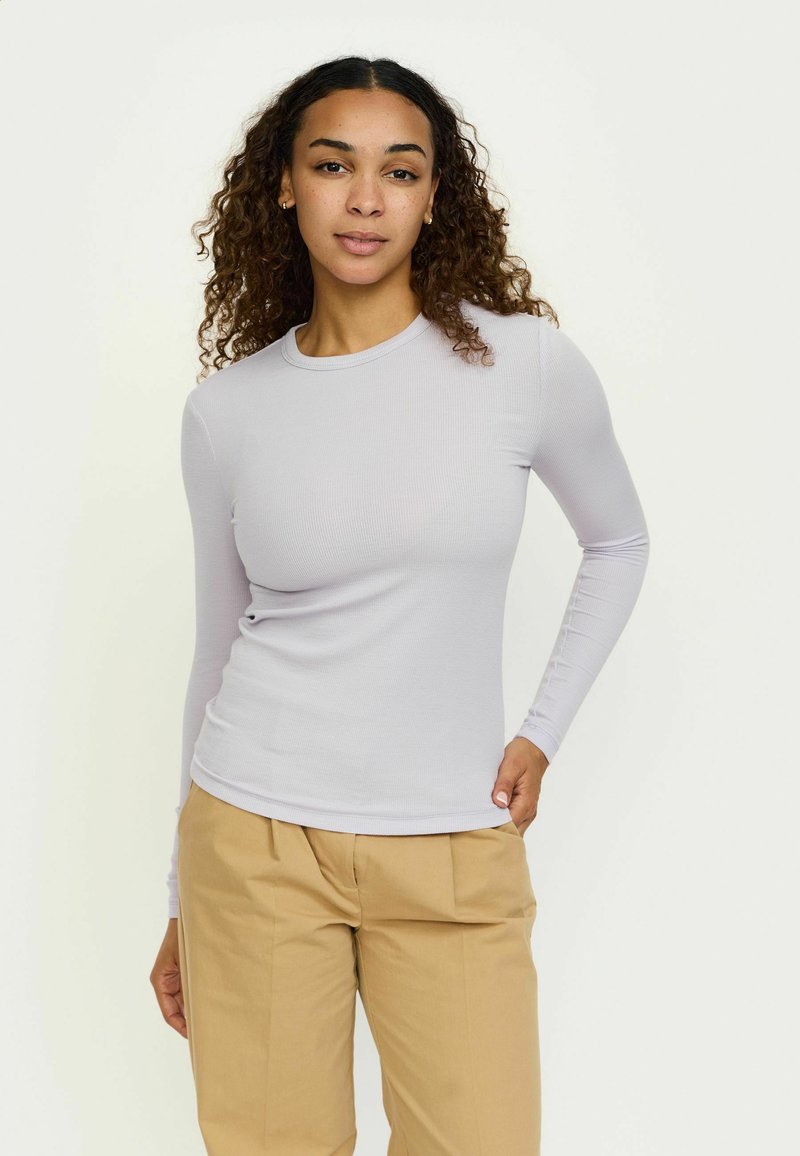 Helllila Langarmshirt mit geripptem Design, taillierte Passform, Rundhalsausschnitt, kombiniert mit beigen Hosen.