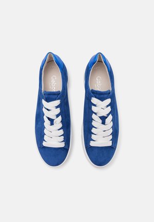 Par de zapatillas de ante azul con cordones blancos y suelas blancas, vistas desde arriba sobre un fondo blanco.