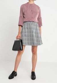 Blusa rosa de botones con mangas acampanadas; falda A-line de cuadros grises; bolso negro con herrajes plateados; zapatos negros con cordones.