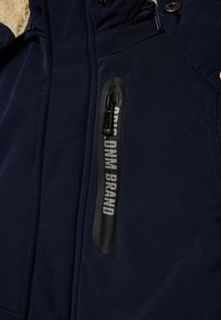 Chaqueta azul marino con un interior suave y texturizado, un bolsillo con cremallera negra con marca, y detalles de hardware a presión en el collar.