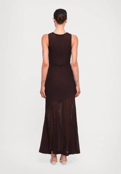 Brown ribbed maxi dress with sleeveless design, an asymmetrical hemline, and a fitted waist, made from a lightweight textured material.