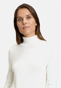 Weißer Rollkragenpullover aus weichem Strickstoff. Enganliegendes Design mit langen Ärmeln und geripptem Kragen. Glatte Textur, minimalistische Details.