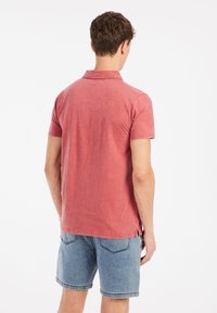 Rode poloshirt van textuurstof, met een klassieke kraag en korte mouwen, gecombineerd met denim shorts, gezien vanuit de achterkant.