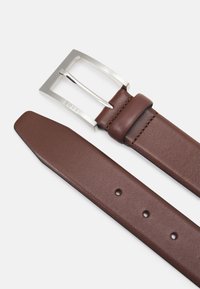 Ceinture en cuir marron avec boucle métallique argentée, de forme rectangulaire, texture lisse, et cinq trous d'ajustement. Nom de la marque estampé.