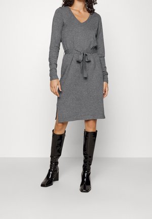 Woman wearing a knee-length, long-sleeve gray knit dress with a waist tie and black shiny knee-high boots, standing on a plain background.