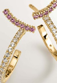 Pendientes de aro de oro que presentan una fila de piedras rosas en la parte superior y piedras transparentes a lo largo de los lados. Acabado de metal liso con un aspecto pulido.