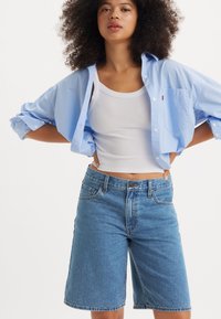 Blå denimshorts med en avslappet passform, med knappestenging, frontlommer og en jevn tekstur. Kombinert med en hvit tank topp og en lys blå knappet skjorte.