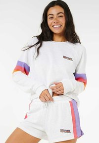 Sweatshirt blanc avec des manches rayées multicolores et le logo "RIPCURL". Assorti à un short blanc avec des accents colorés sur les côtés.
