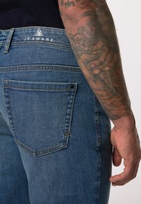 Jeans de mezclilla azul oscuro con un corte slim, que presentan un bolsillo trasero con un acento en forma de triángulo, costuras sutiles y un logo por encima de la cinturilla.