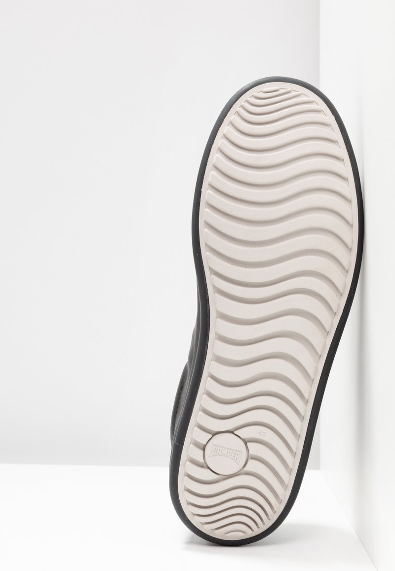 Schwarze Schuhsohle mit einer weißen Gummibasis. Verfügt über ein wellenförmiges Profilmuster und ein kreisförmiges Logo. Die Seitenansicht zeigt ein geschwungenes Design.