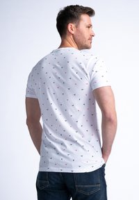 Bílý tričko s krátkým rukávem, které má rozptýlený vzor malých červených a černých tvarů. Vyrobeno z bavlny, má přiléhavý střih.