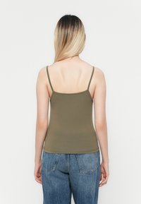 Top sin mangas de color verde oliva, confeccionado en un material suave, con tirantes finos y un diseño ajustado, combinado con jeans de mezclilla azul de cintura alta.