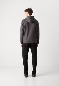 Felpa grigia con un design aderente e cappuccio regolabile, abbinata a pantaloni neri. Il tessuto appare morbido ed elastico.