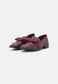 Mocassins bordeaux en matériau brillant à motif crocodile, avec accent de nœud élastique et petit talon empilé. Texture lisse et design à bout pointu.