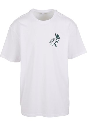 Fehér pamut póló zöld virágmintával és pillangó díszítéssel a bal mellrészen; rövid ujjú és kerek nyakkivágású.
