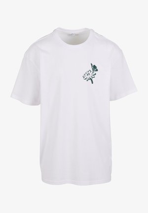 Fehér pamut póló zöld virágmintával és pillangó díszítéssel a bal mellrészen; rövid ujjú és kerek nyakkivágású.