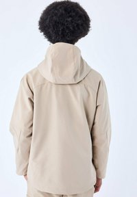 Chaqueta con capucha beige de superficie texturizada, corte holgado y mangas largas. Presenta un alto cuello y detalles de costura sutiles.
