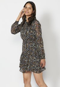 Schwarzes Kleid mit floralem Muster, mit langen durchsichtigen Ärmeln, gerafftem Saum und tailliertem Oberteil. Leichter, blickdichter Stoff.