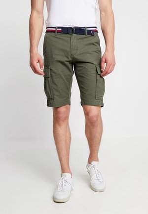 Khaki zielone spodenki cargo wykonane z bawełny, z wieloma bocznymi kieszeniami i podwiniętym dołem. Noszone z białą koszulką i białymi sneakerami.