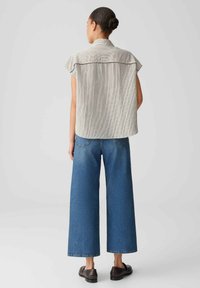 Camicetta a maniche corte a righe in bianco e nero, con una vestibilità comoda, abbinata a jeans blu a gamba larga e scarpe scure. Design semplice, stile informale.